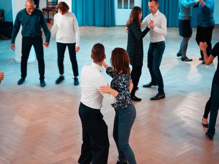 Des couples dansent le tango dans une salle lumineuse au parquet, chez BE-TANGO.
