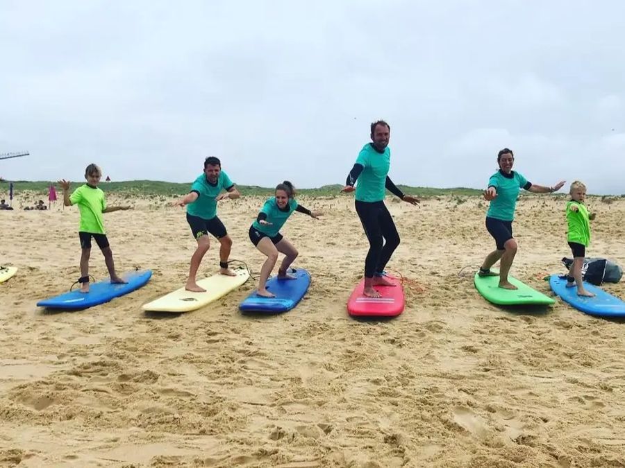 Des enfants et des adultes s’entraînent à se lever sur des planches de surf posées sur le sable.
